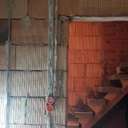 Instalacja elektryczna w surowym stanie: kable w peszlach prowadzone po ścianie z pustaków ceramicznych, widoczne pomarańczowe puszki podtynkowe, fragment schodów w tle.