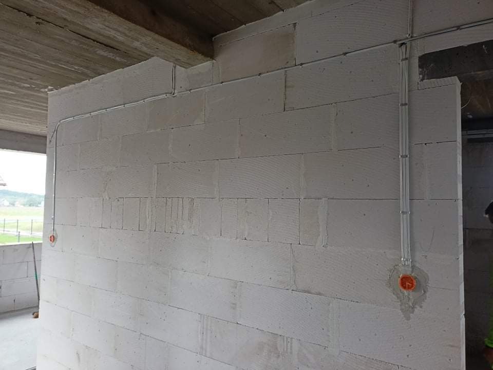 Ściana z betonu komórkowego z poprowadzonymi przewodami elektrycznymi w peszlach i zamontowanymi puszkami instalacyjnymi w kolorze pomarańczowym.