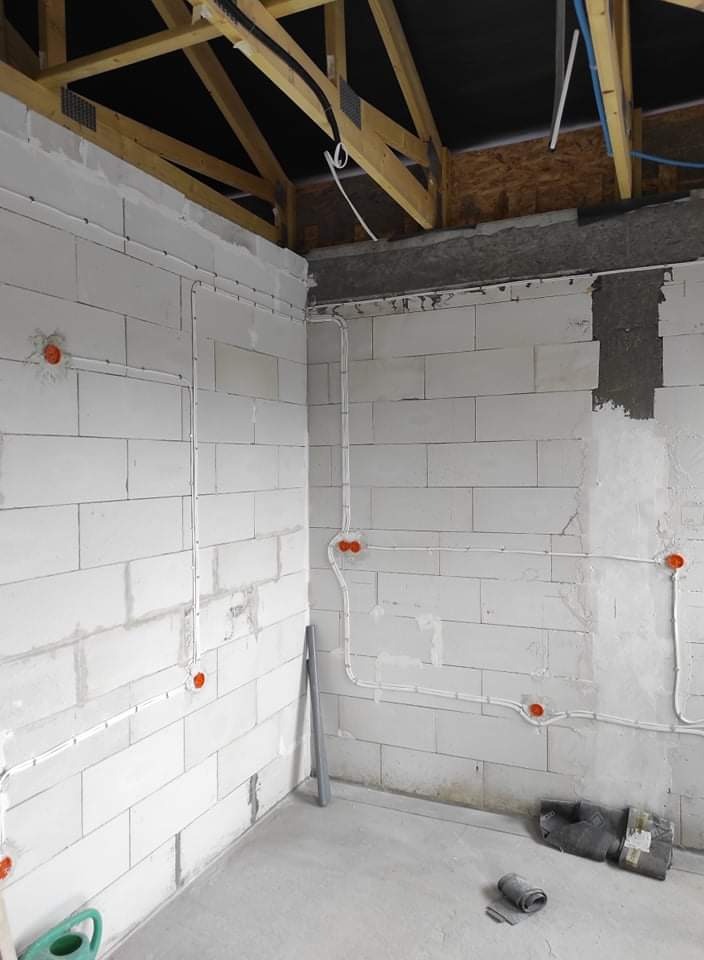 Wewnętrzne okablowanie elektryczne w surowym stanie, widoczne kable i puszki na ścianach z betonu komórkowego, surowe wykończenie, widoczna konstrukcja dachu.