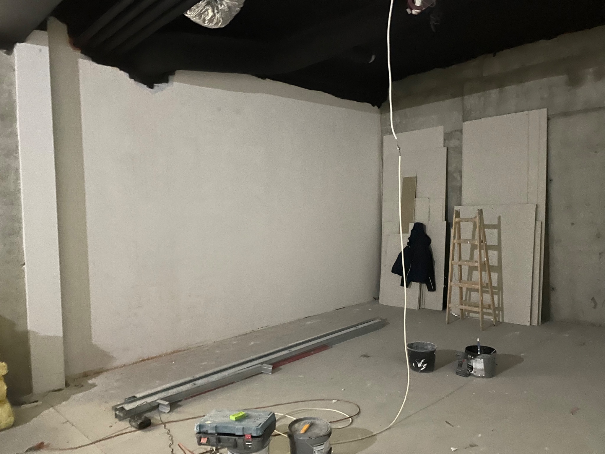 Przygotowanie do montażu sufitu z płyt karton gips, widoczne profile, narzędzia, płyty gipsowe oparte o ścianę i drabina.