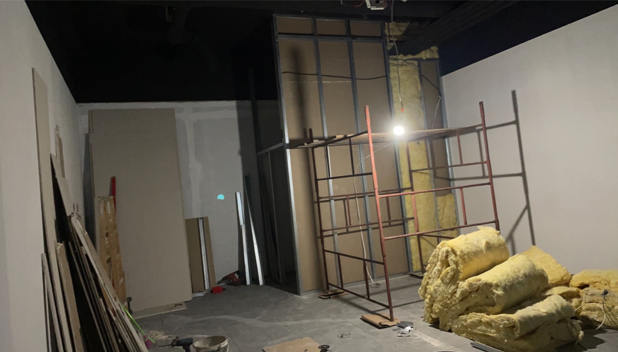 Wnętrze w trakcie prac wykończeniowych: metalowy szkielet ściany z izolacją z wełny mineralnej, widoczne płyty gipsowo-kartonowe i rusztowanie.