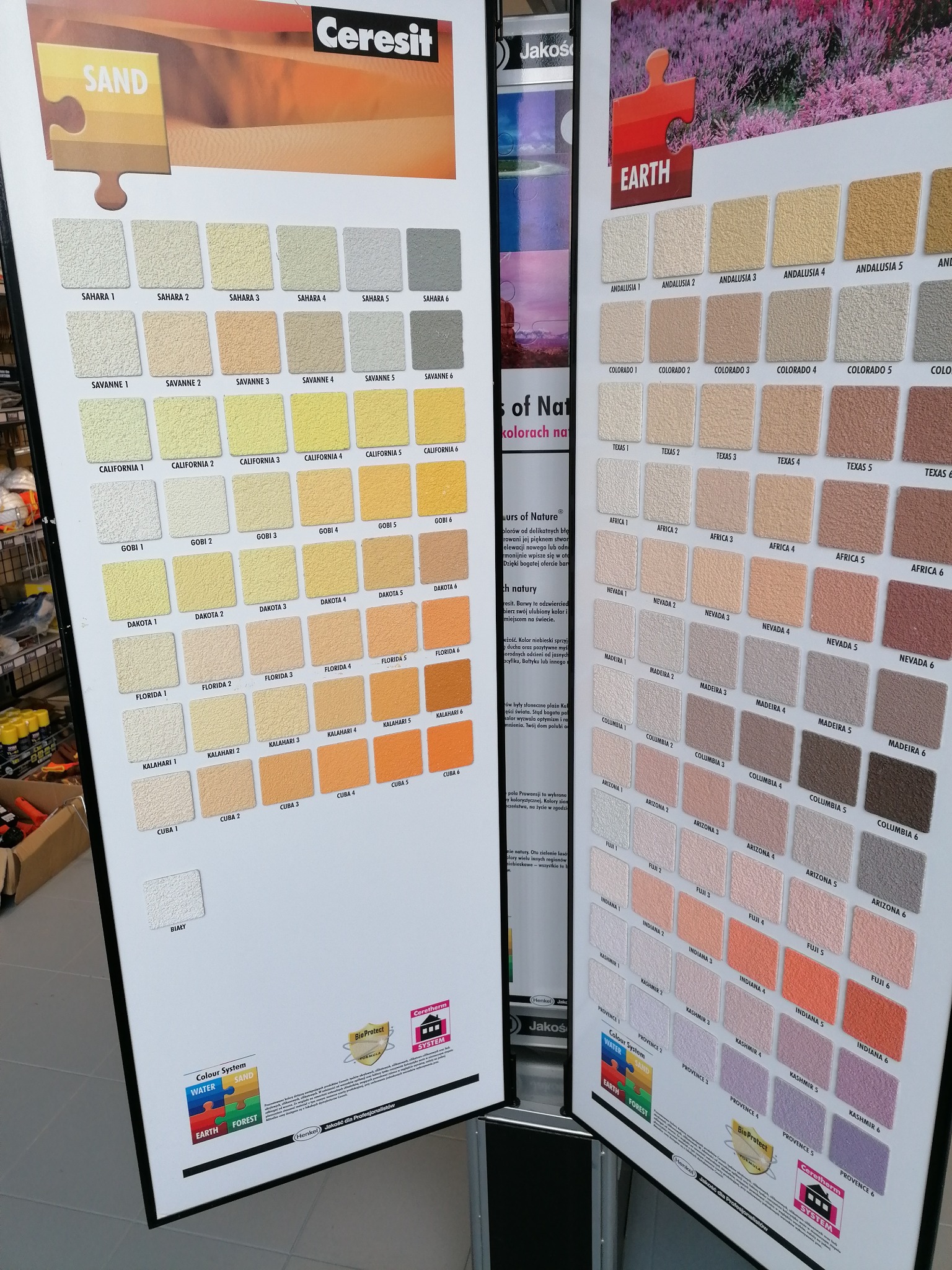 Ekspozycja próbek tynków dekoracyjnych w różnych odcieniach, podzielonych na dwie palety kolorystyczne: 'Sand' z beżami i żółcieniami oraz 'Earth' z brązami i różami, prezentowane na planszach...