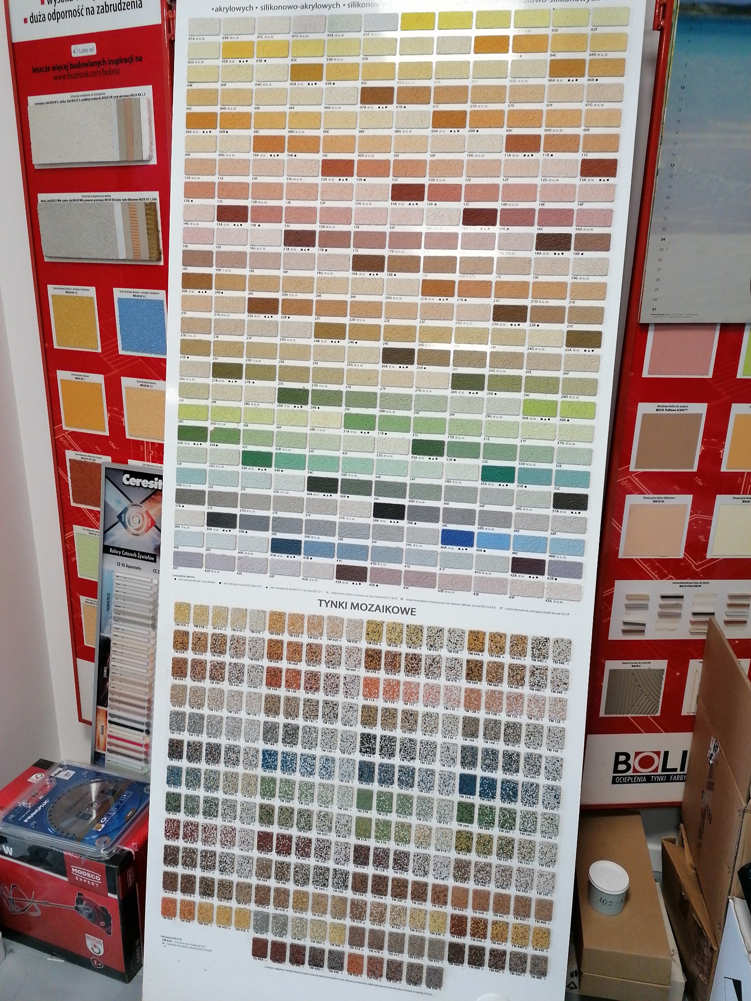 Paleta kolorów i struktur tynków akrylowych, silikonowo-akrylowych i mozaikowych, prezentowana na planszy z oznaczeniami producenta Bolix, obok widoczny mikser do zapraw Modeco Expert...