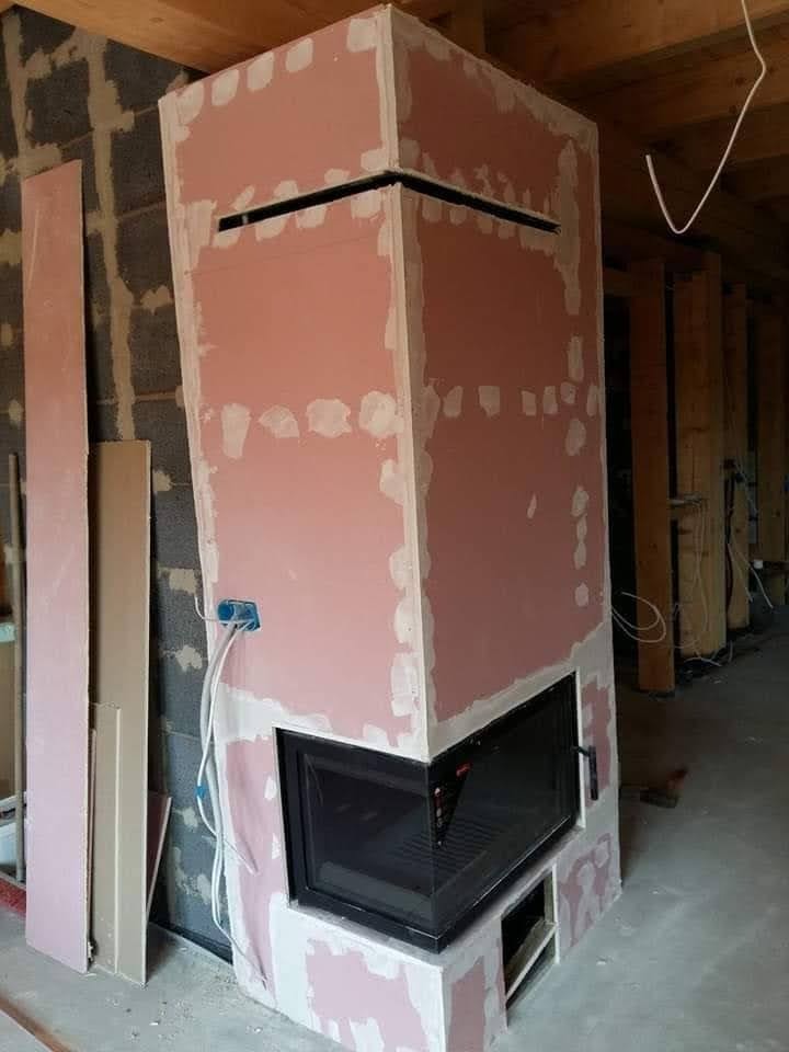 Konstrukcja kominka z płyt kartonowo-gipsowych w trakcie szpachlowania, widoczne łączenia płyt i otwór na wkład kominkowy, surowy stan wykończenia.