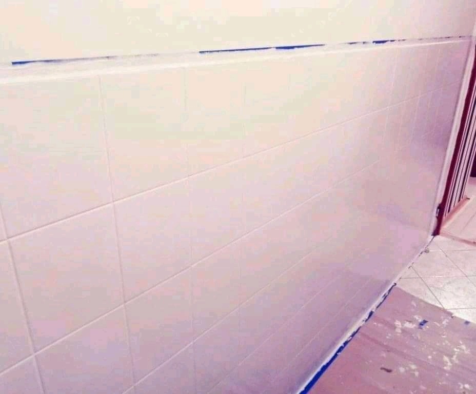 Ściana wyłożona białymi, prostokątnymi płytkami w trakcie fugowania w Rudnie, zabezpieczona niebieską taśmą malarską przy suficie i podłodze.