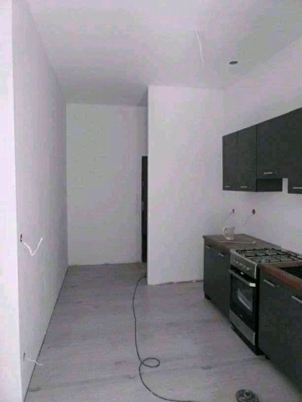 Wnętrze remontowanej kuchni z szarymi szafkami, świeżo pomalowanymi ścianami na biało, widocznymi przewodami elektrycznymi i szarą podłogą w trakcie prac wykończeniowych.