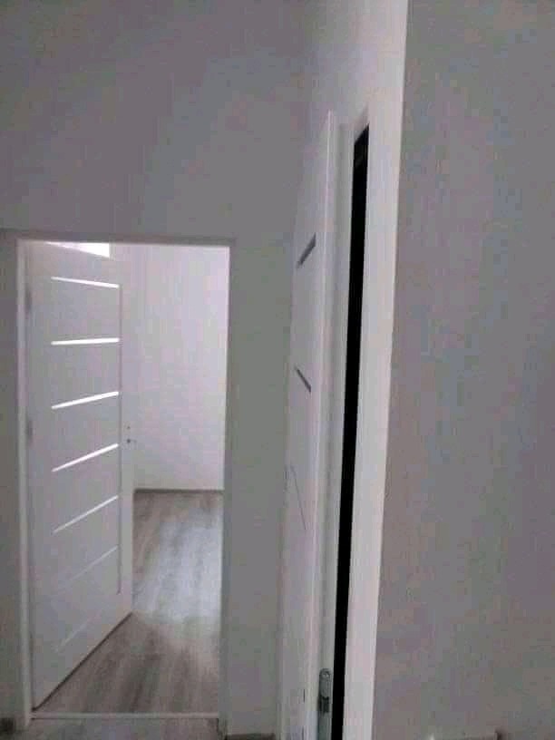 Nowoczesne, białe drzwi wewnętrzne z poziomymi frezowaniami, częściowo otwarte, widok na jasne pomieszczenie z panelami podłogowymi.