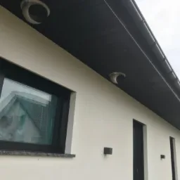 Zewnętrzne nawiewniki rekuperacji zamontowane pod okapem budynku w Maczkowie, widoczne okno z czarną ramą i czarne drzwi.