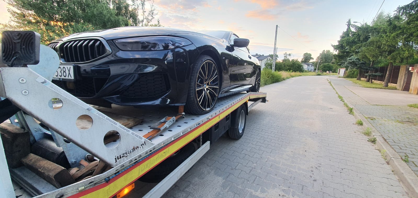 Czarny samochód BMW na srebrnej lawecie z żółtymi pasami, widok z boku na tle drogi i drzew.