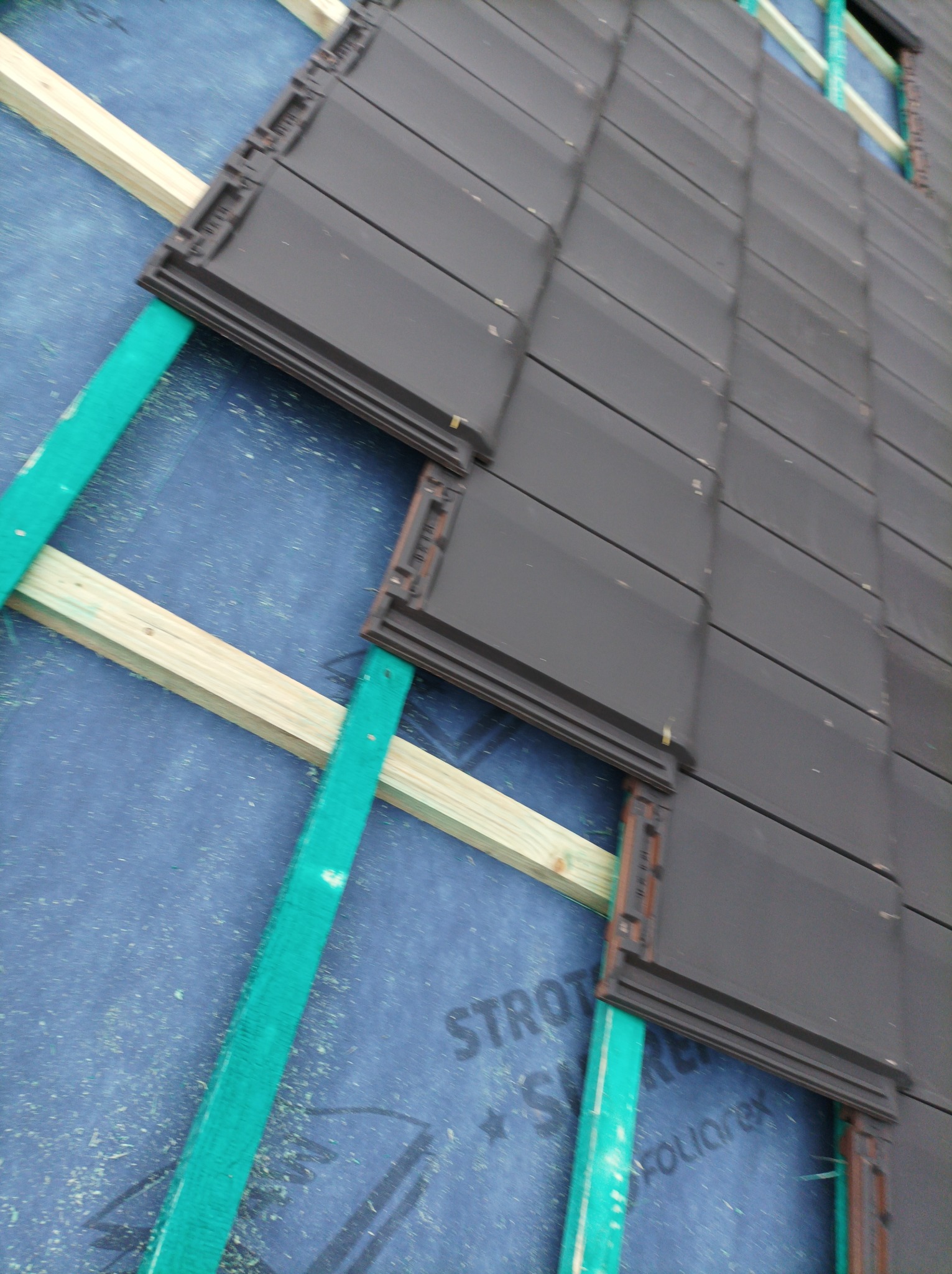 Montaż ciemnoszarej dachówki ceramicznej na łatach i kontrłatach, widoczna membrana dachowa z nadrukiem producenta.