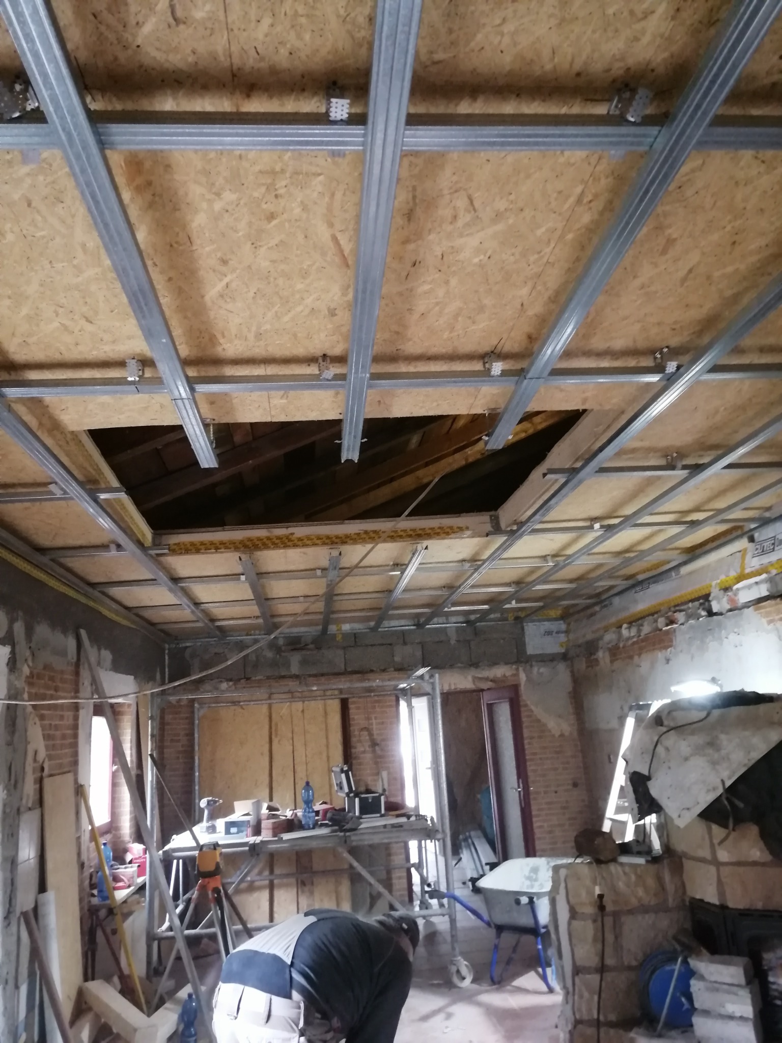 Montaż metalowej konstrukcji sufitu podwieszanego w surowym wnętrzu z odsłoniętą cegłą i widocznym otworem w stropie