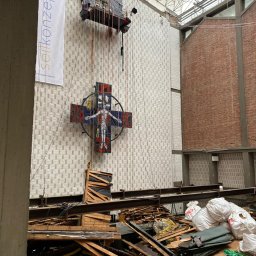 Usługi budowlane - Demontaż witraża krzyża w kościele z użyciem platformy wiszącej. Widoczne rusztowania, liny i gruz na drewnianej podłodze. Prace na wysokościach.