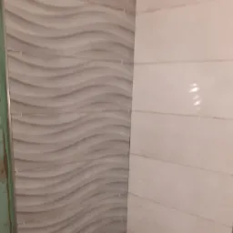 Ściana wyłożona dwoma rodzajami płytek: szare płytki z falistym wzorem i beżowe płytki ułożone poziomo, widoczne krzyżyki dystansowe.