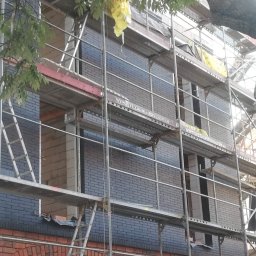 Wojciech Chałubowicz - Budynek w Chojnicach w trakcie murowania z wykorzystaniem rusztowania, widoczne cegły w dwóch odcieniach.