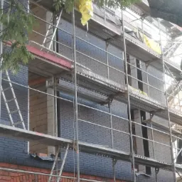 Budynek w Chojnicach w trakcie murowania z wykorzystaniem rusztowania, widoczne cegły w dwóch odcieniach.