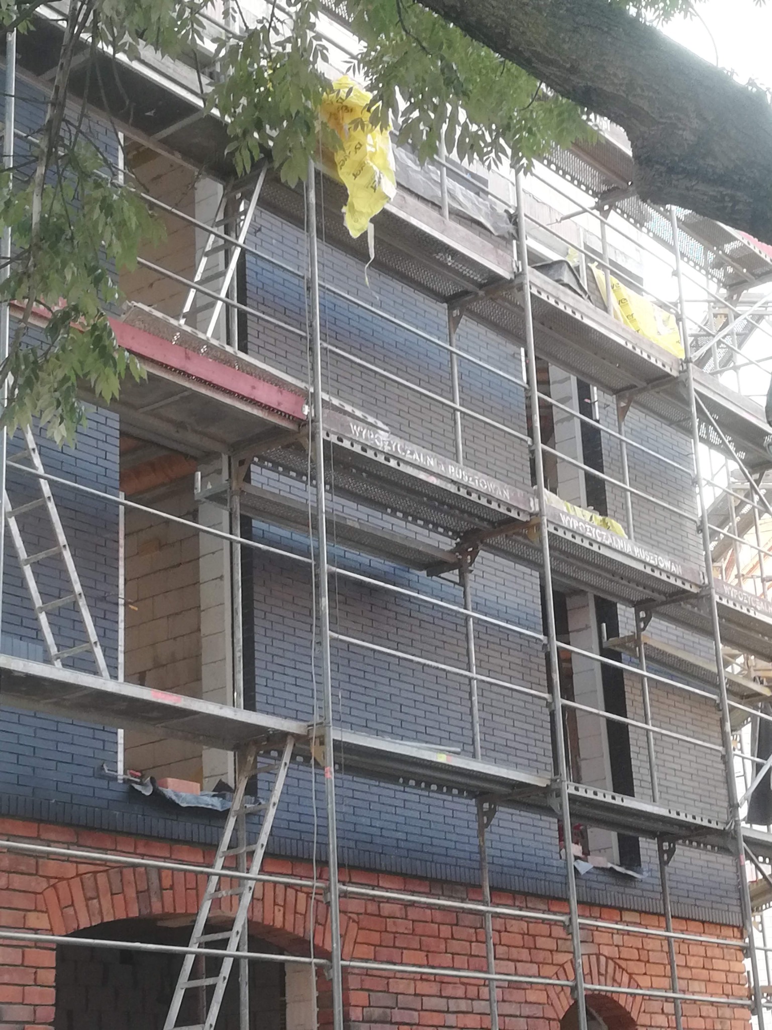 Budynek w Chojnicach w trakcie murowania z wykorzystaniem rusztowania, widoczne cegły w dwóch odcieniach.