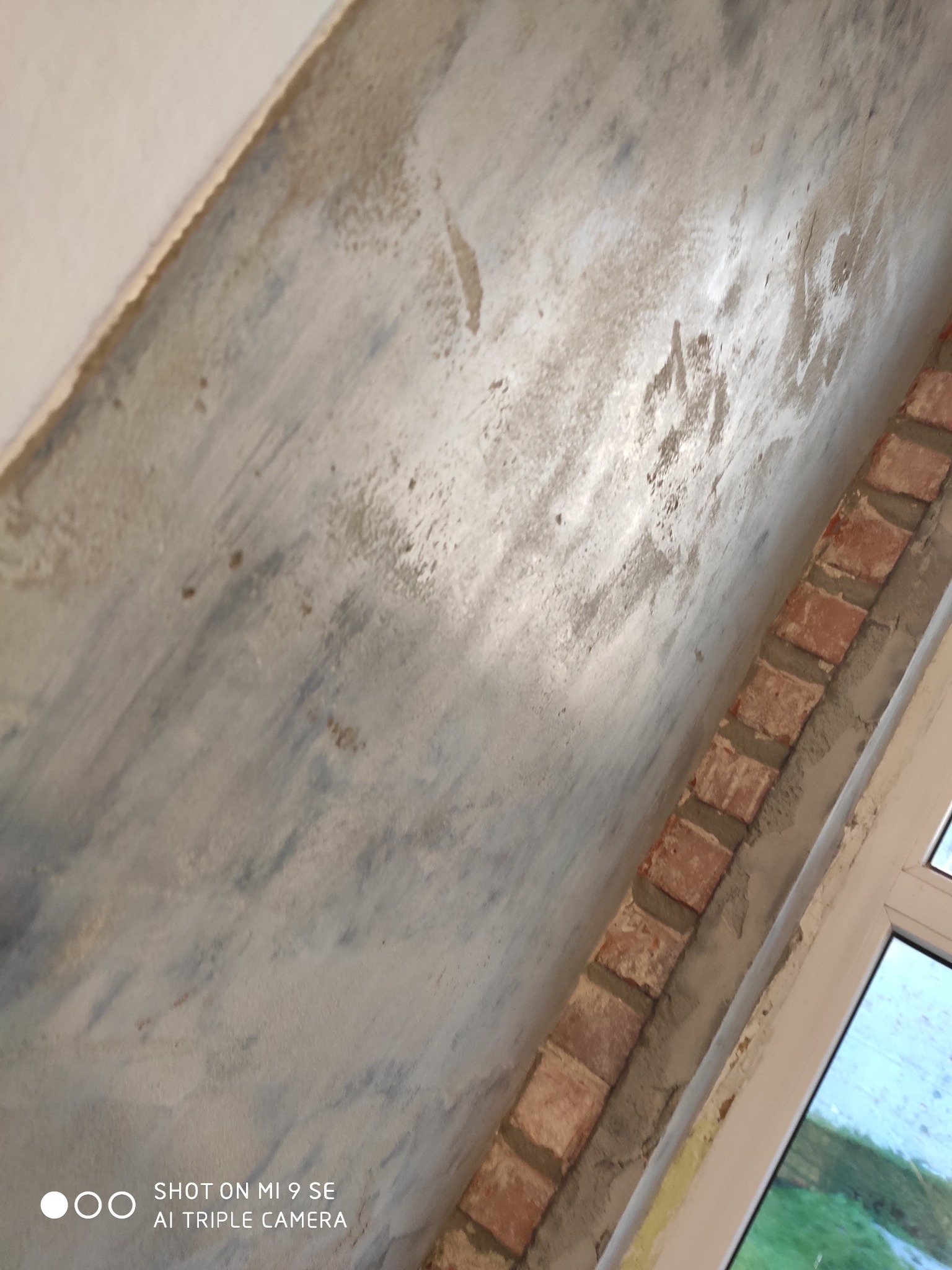 Surowa ściana z fragmentem dekoracyjnego muru z czerwonej cegły, widoczne ślady po malowaniu, ujęcie z dołu.