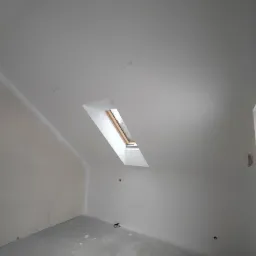 Poddasze z oknem dachowym po nałożeniu gładzi, widoczne niedoskonałości na podłodze i ścianach przed dalszym wykończeniem.