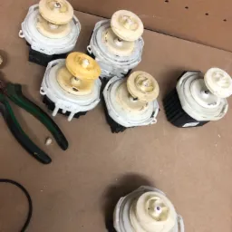 Pumpy do pralek, niektóre z żółtymi wirnikami, ułożone na warsztatowym stole w Osielsku, obok leżą szczypce i uszczelka.