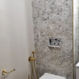 Nowoczesna toaleta wisząca z złotymi akcentami, bidetką i uchwytem na papier toaletowy na tle płytek w stylu vintage.