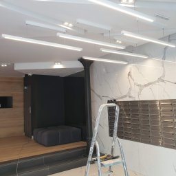Usługi remontowe - Nowoczesne oświetlenie sufitowe w holu budynku z marmurową ścianą, skrzynkami pocztowymi i drabiną malarską