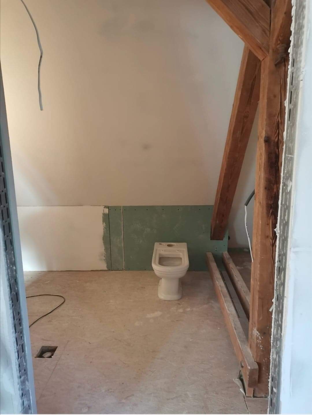 Łazienka w trakcie remontu na poddaszu: surowe ściany z płyt gipsowo-kartonowych, biały bidet na surowej podłodze, widoczne drewniane elementy konstrukcyjne dachu.