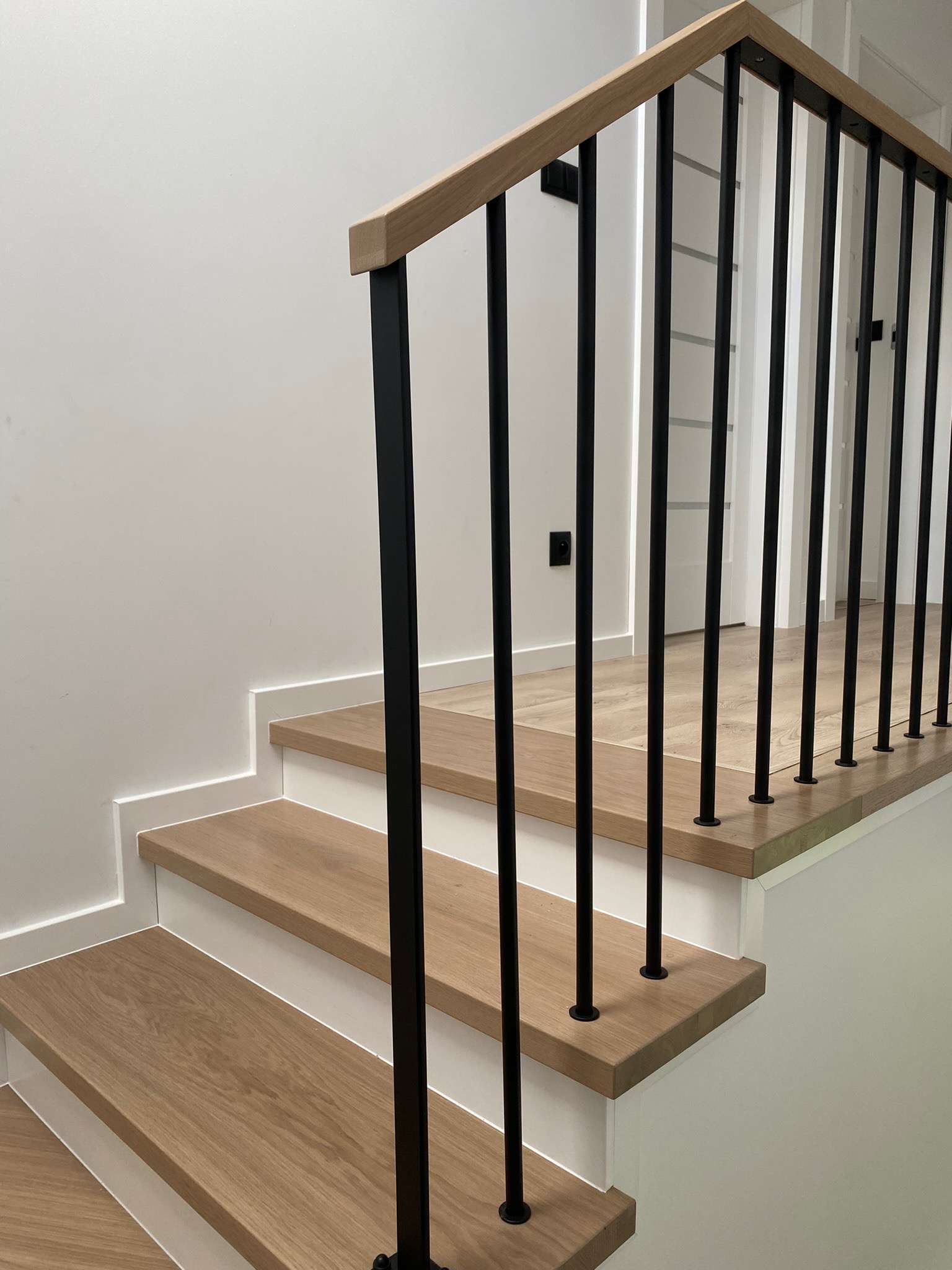 Nowoczesne schody z drewnianymi stopniami i czarnymi, metalowymi balustradami, widok z dołu, minimalistyczny design, białe ściany, jasne drewno.