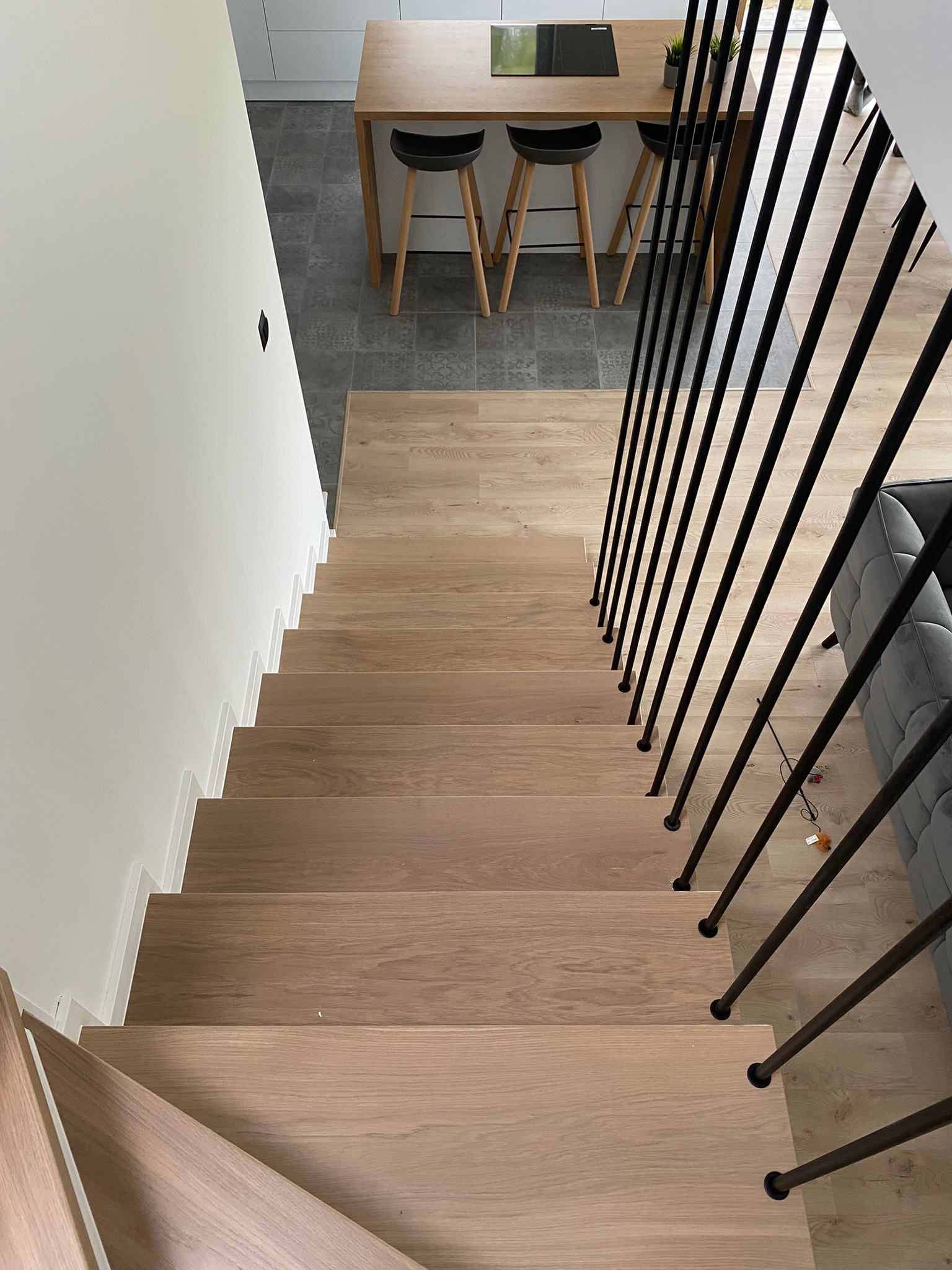 Nowoczesne schody drewniane z czarnymi, pionowymi balustradami, widok z góry na jasne drewno stopni i minimalistyczny design.