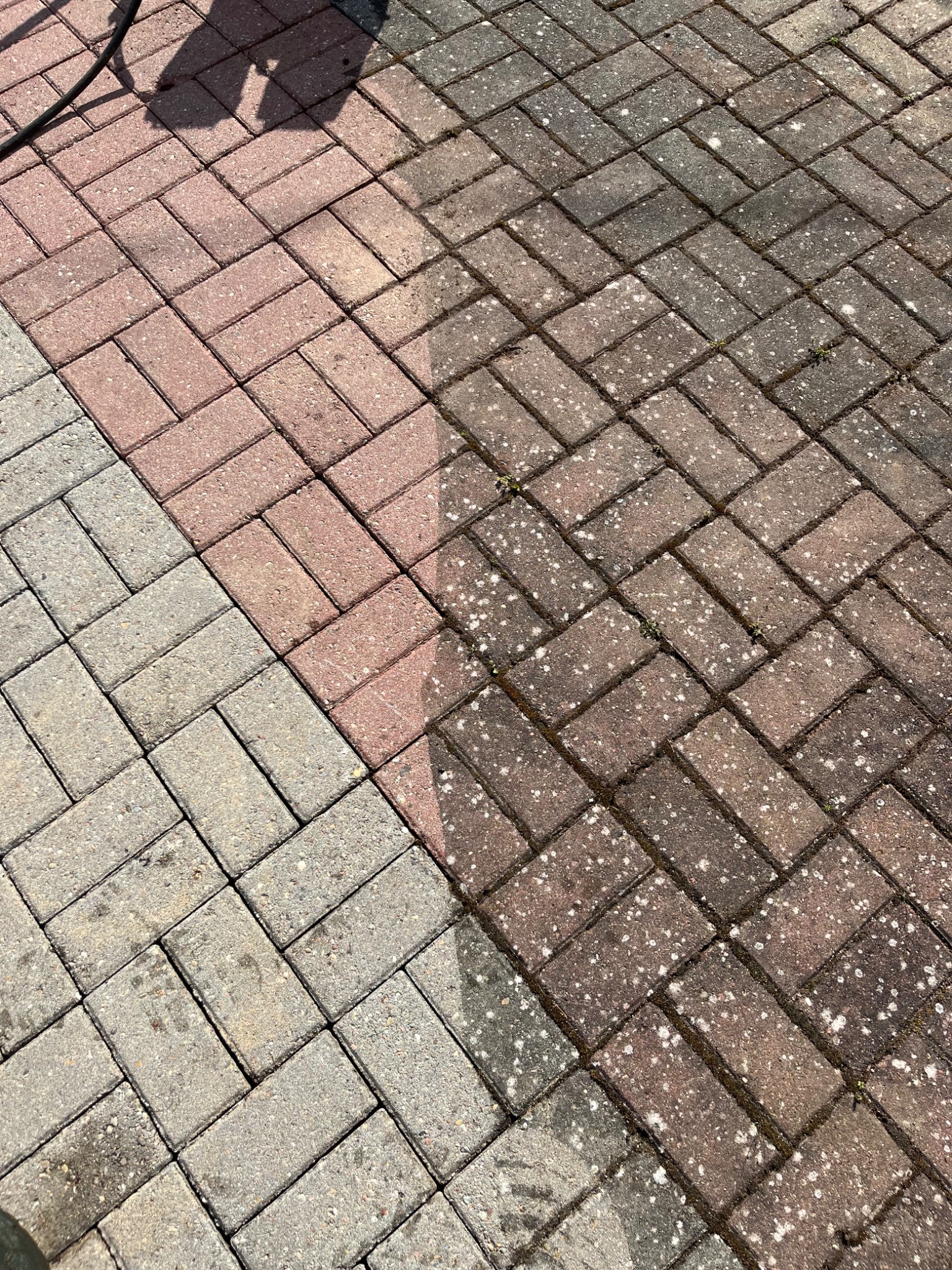 Częściowo wyczyszczona kostka brukowa ułożona w jodełkę, widoczna różnica w kolorze między czystą a brudną powierzchnią.