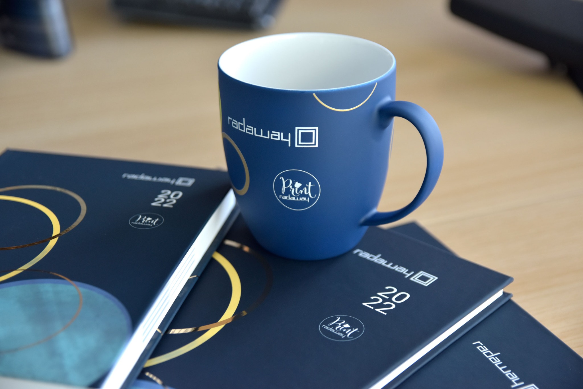 Niebieski kubek z nadrukiem logo firmy 'radaway' i kalendarze firmowe 2022 z elementami graficznymi w kolorze złotym.