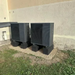 Dwie pompy ciepła powietrze-woda zamontowane na betonowych podstawach z wysypanym drobnym żwirem, zainstalowane przy ścianie budynku w Bydgoszczy.