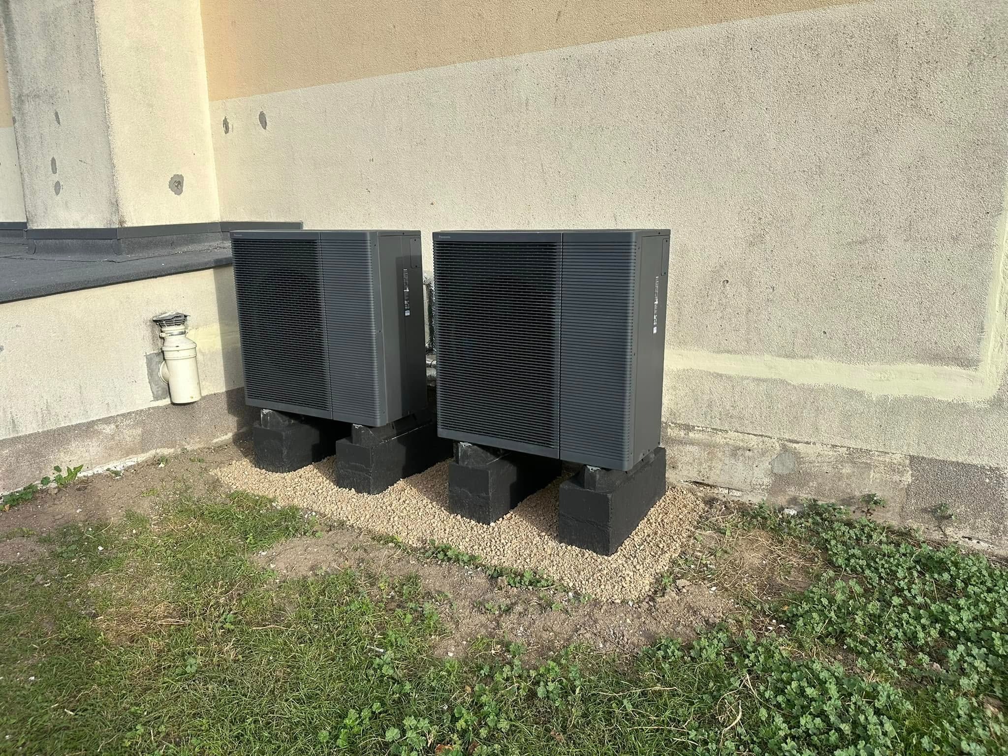 Dwie pompy ciepła powietrze-woda zamontowane na betonowych podstawach z wysypanym drobnym żwirem, zainstalowane przy ścianie budynku w Bydgoszczy.