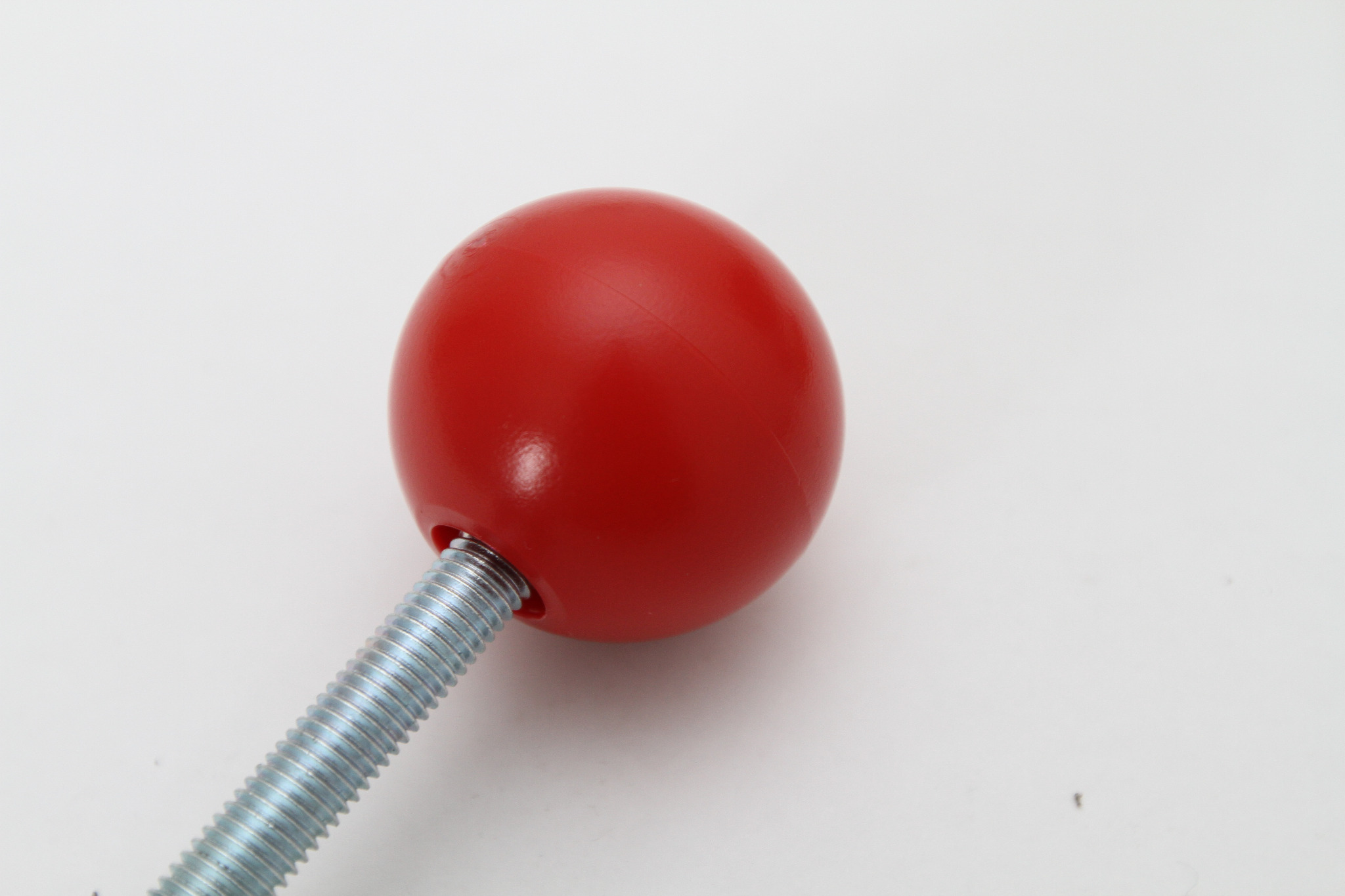 Czerwona, kulista rączka z gwintowanym trzpieniem, element konstrukcyjny urządzenia zabawowego.