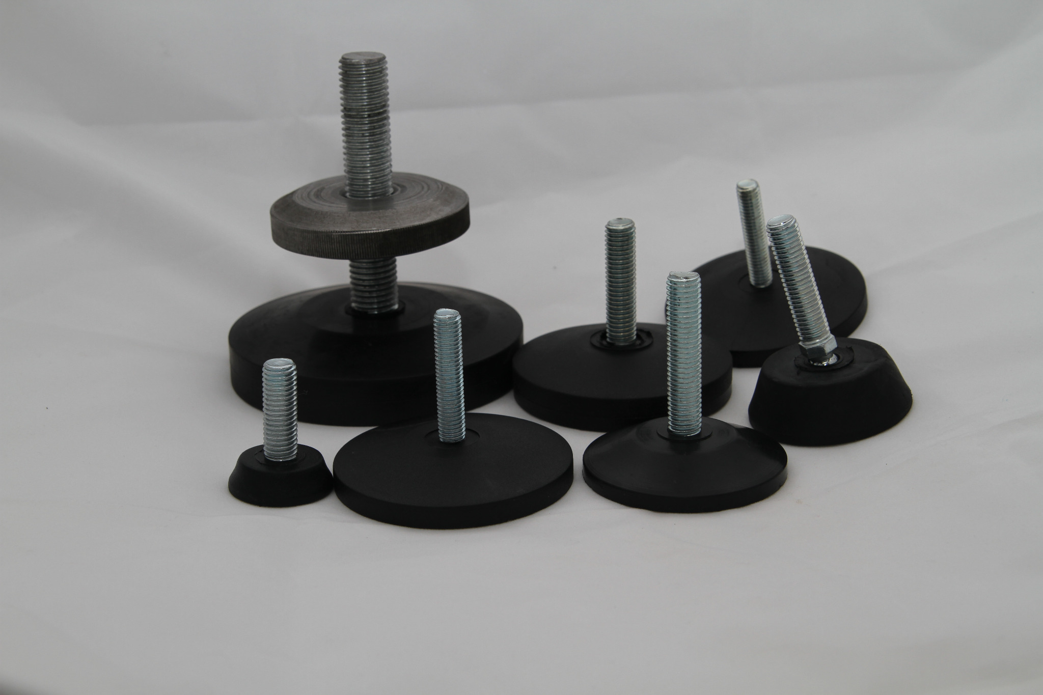 Zestaw regulowanych stopek do placu zabaw, z gwintowanymi trzpieniami i czarnymi, gumowymi podstawami o różnych rozmiarach, na białym tle.