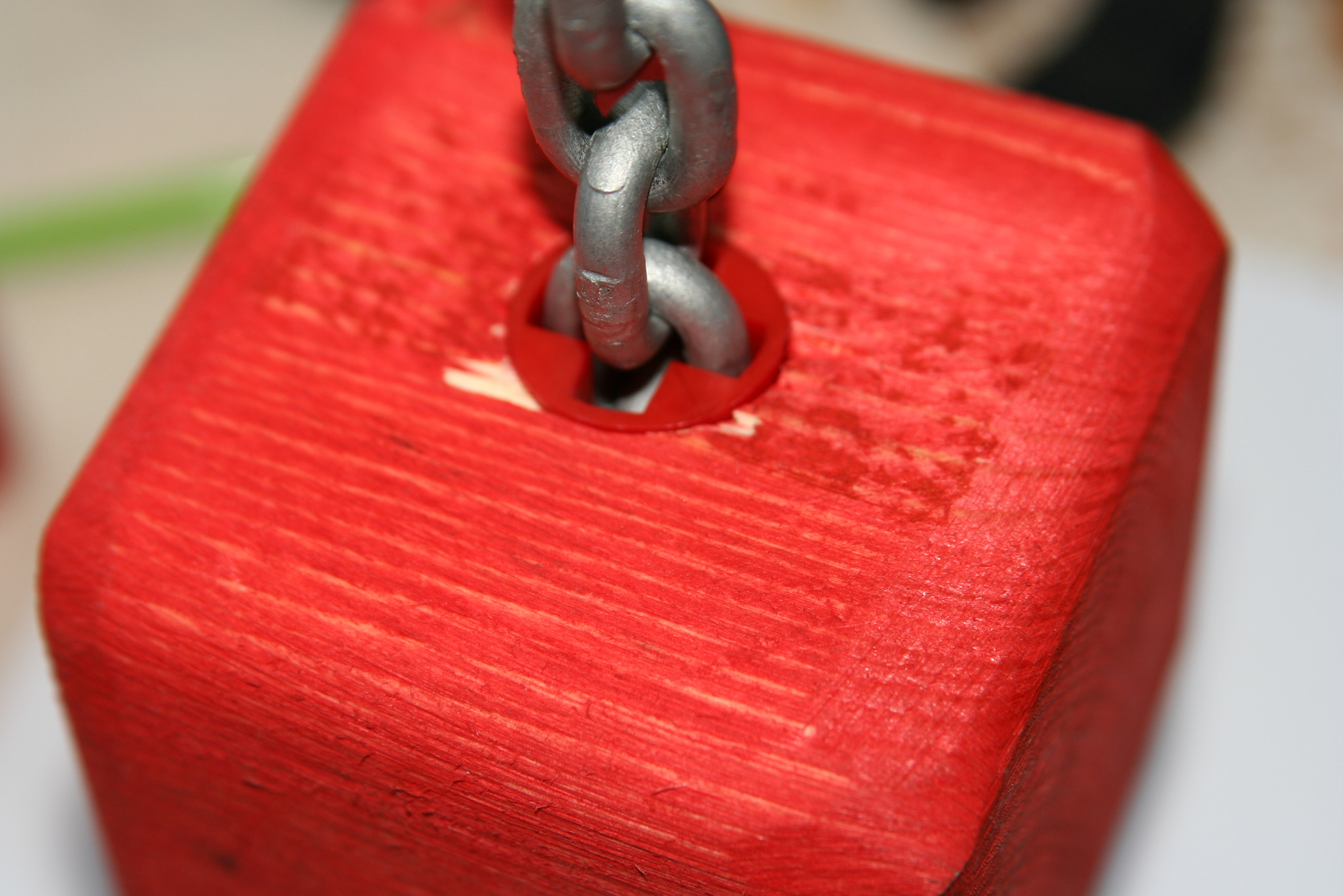 Czerwony, drewniany sześcian z metalowym łańcuchem przechodzącym przez otwór, zbliżenie.