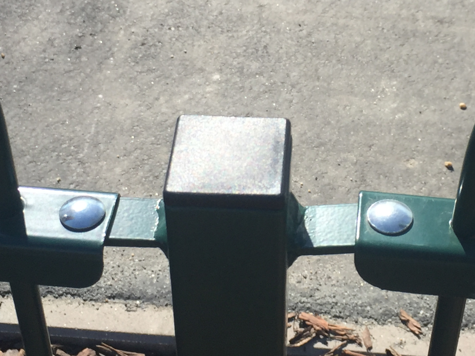 Detale konstrukcyjne zielonego, metalowego ogrodzenia placu zabaw we Wrocławiu, z widocznymi nitami i kwadratowym zakończeniem słupka.