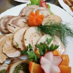 Dekoracyjnie ułożone na białym talerzu roladki mięsne z r&oacute;żnymi nadzieniami, ozdobione pomarańczami, rzodkiewką, marchewką, koperkiem i natką pietruszki.