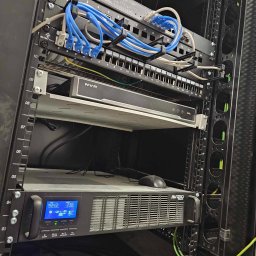 M-Instal - Szafa rack z zainstalowanym sprzętem sieciowym: switch, rejestrator NVR i zasilacz awaryjny UPS marki Avizio, okablowanie sieciowe z niebieskimi kablami Ethernet, przewody uziemiające w kolorze...
