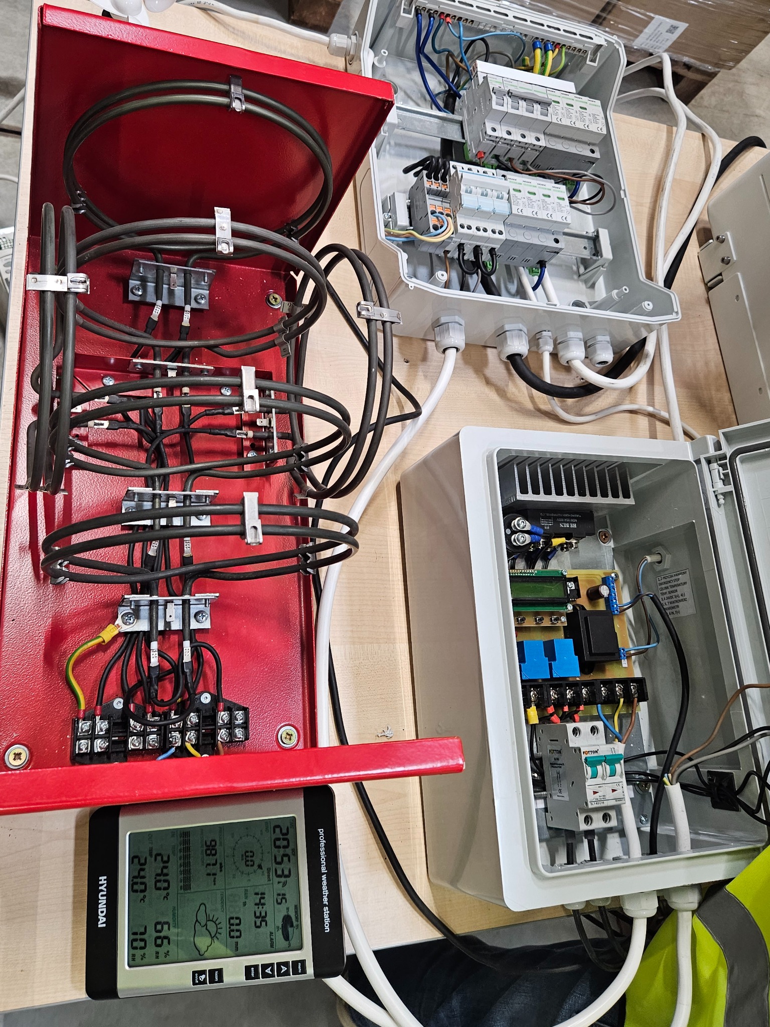 Otwarte skrzynki elektryczne z widocznymi przewodami, bezpiecznikami i elementami sterującymi, obok stacji pogodowej Hyundai, ukazującej aktualne parametry atmosferyczne.