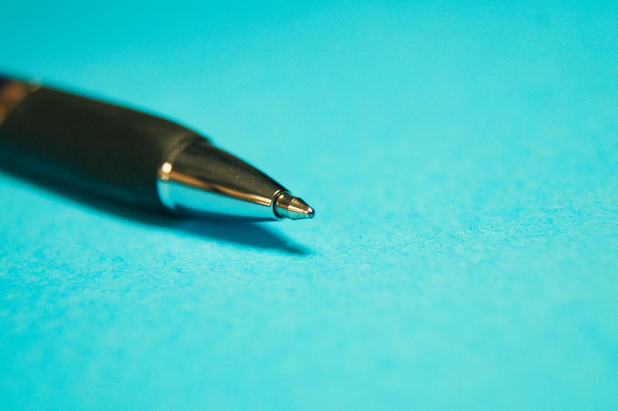 Zbliżenie czarnego długopisu z metalową końcówką na teksturowanym, turkusowym tle.
