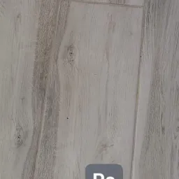Jasnoszare panele podłogowe imitujące drewno, widoczne z bliska, z ciemniejszymi smugami i sękami, opatrzone znakiem wodnym 'Po'.