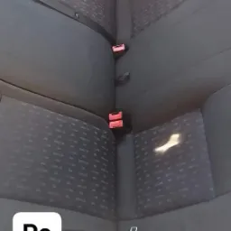 Wnętrze samochodu z wyczyszczoną tylną kanapą o ciemnej tapicerce w drobny wzór, widoczne zagłówki i pasy bezpieczeństwa z czerwonymi klamrami, jasne plamy po czyszczeniu na siedzisku.