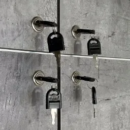 Klucze do szafek pracowniczych w biurze w Warszawie, wiszące na szarym tle szafek.