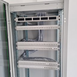 USŁUGI ELEKTRYCZNE MICHAŁ JASIŃSKI - Szary panel krosowniczy z licznymi portami RJ45 i podłączonymi szarymi kablami sieciowymi w szafie rack.