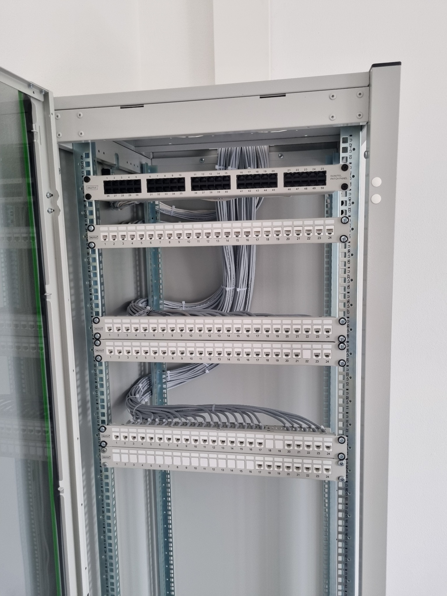 Szary panel krosowniczy z licznymi portami RJ45 i podłączonymi szarymi kablami sieciowymi w szafie rack.