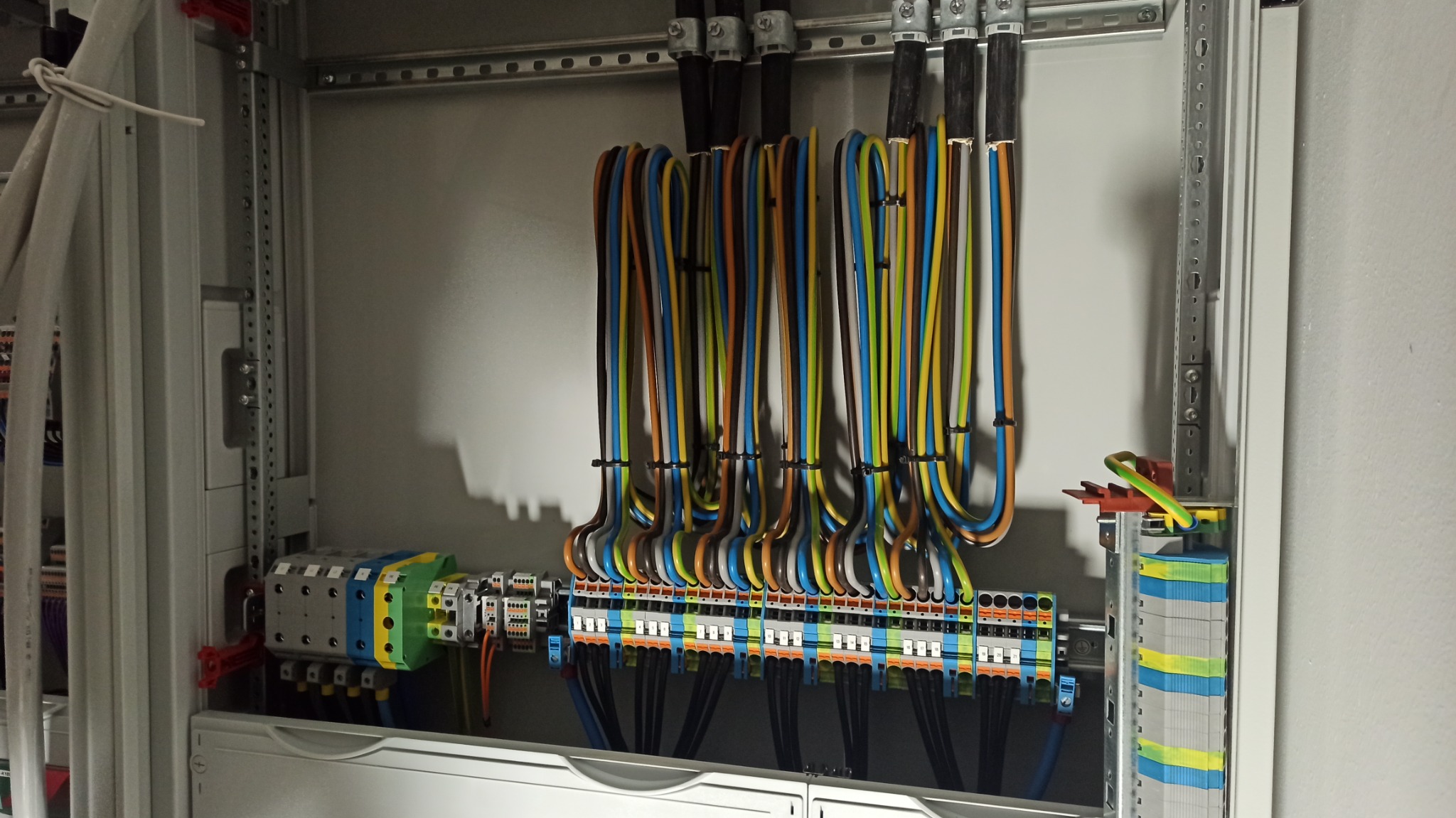 Rozdzielnica elektryczna z podłączonymi kolorowymi przewodami, widoczne listwy zaciskowe i zabezpieczenia, instalacja w trakcie montażu.