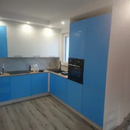 Jasna kuchnia z błękitnymi i białymi frontami szafek, marmurowym backsplashiem, czarnym zlewem i płytą indukcyjną oraz podłogą imitującą drewno; widoczna drabina w rogu.