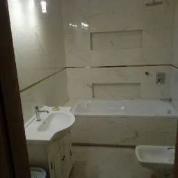 Wykończona łazienka z wanną, umywalką na szafce w stylu retro oraz bidetem i sedesem, wyłożona białymi płytkami imitującymi marmur z poziomymi, złotymi akcentami.