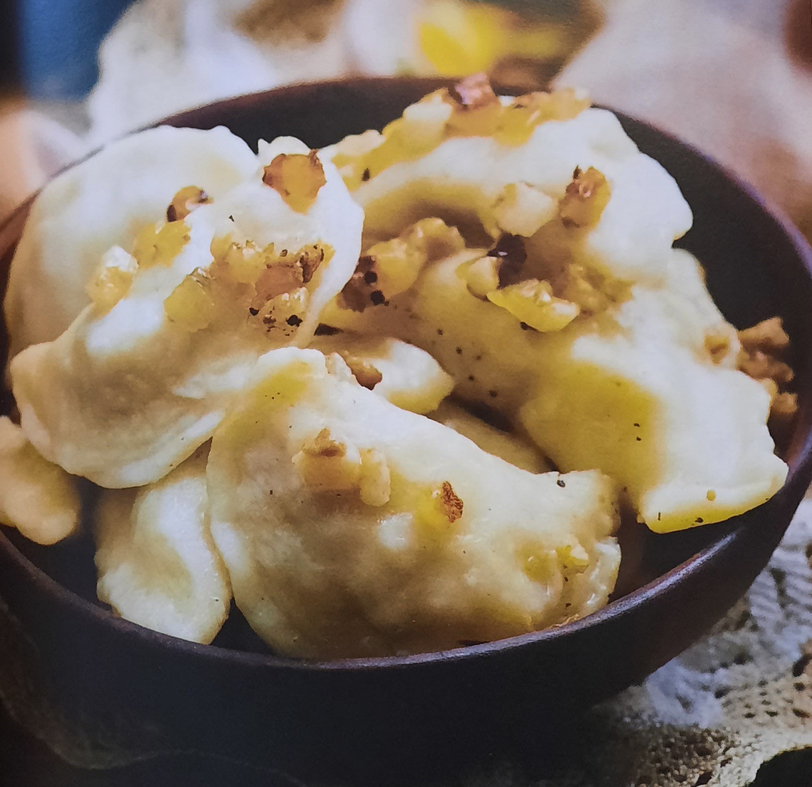 Kluski ziemniaczane polane skwarkami z boczku w ciemnej misce na koronkowej serwetce.