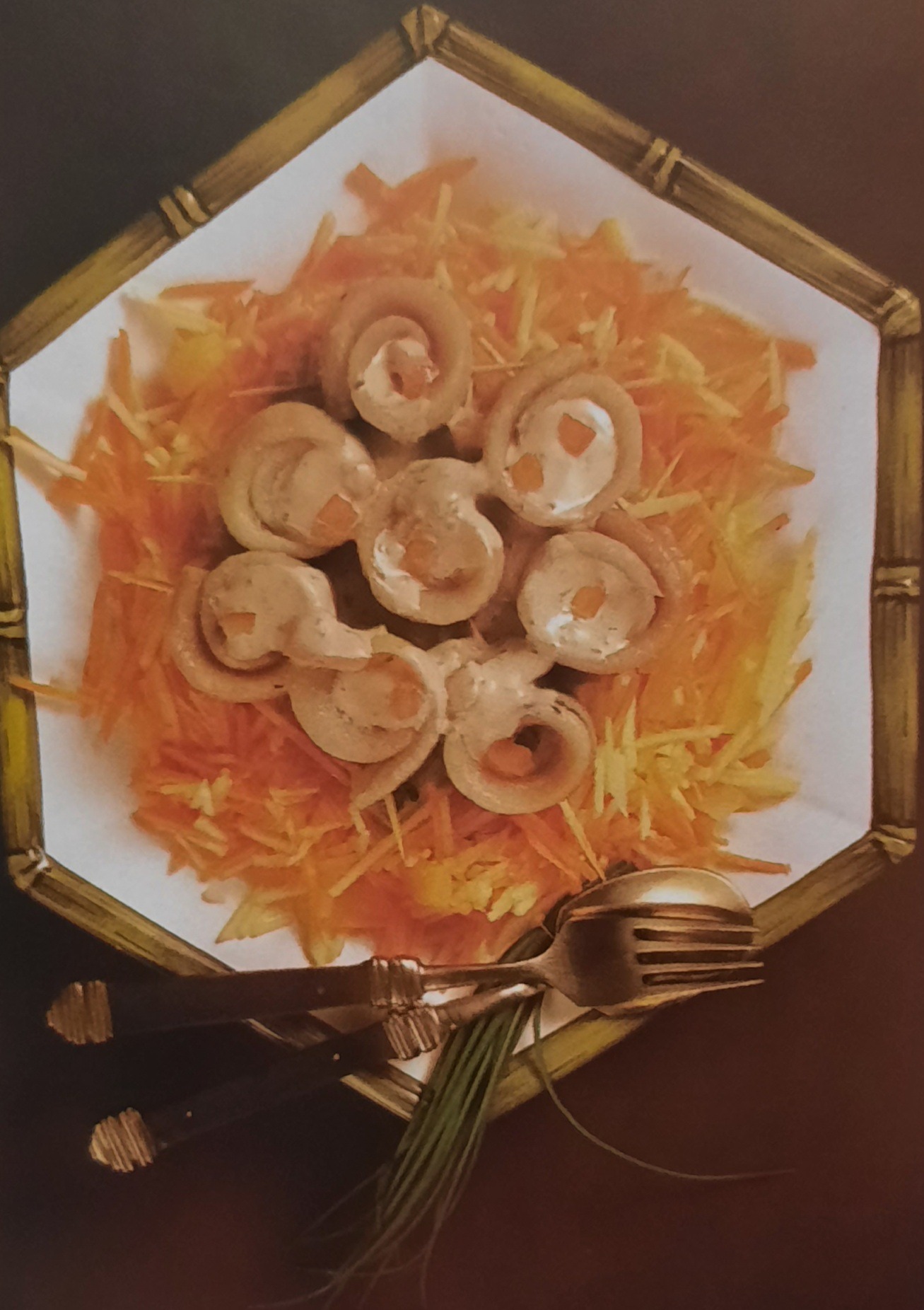 Rolmopsy z kremowym nadzieniem na poszatkowanej marchewce, podane na talerzu w bambusowej ramce z widelcem i szczypiorkiem.